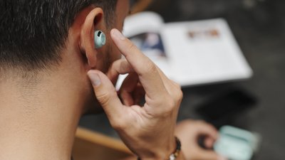 Mann mit In-Ear-Kopfhörer im Ohr tippt zur Bedienung darauf 